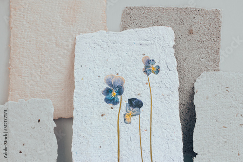 Dried viola flower pressed onto a sheet of handmade paper with a pronounced explicit texture. Reuse of materials.