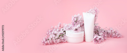 Face and body skin care. A set of cosmetic creams and balms in white tubes and cans on a coral background with sprigs of lilac flowers. Spa treatments for home care. Home rejuvenation and moisturizing