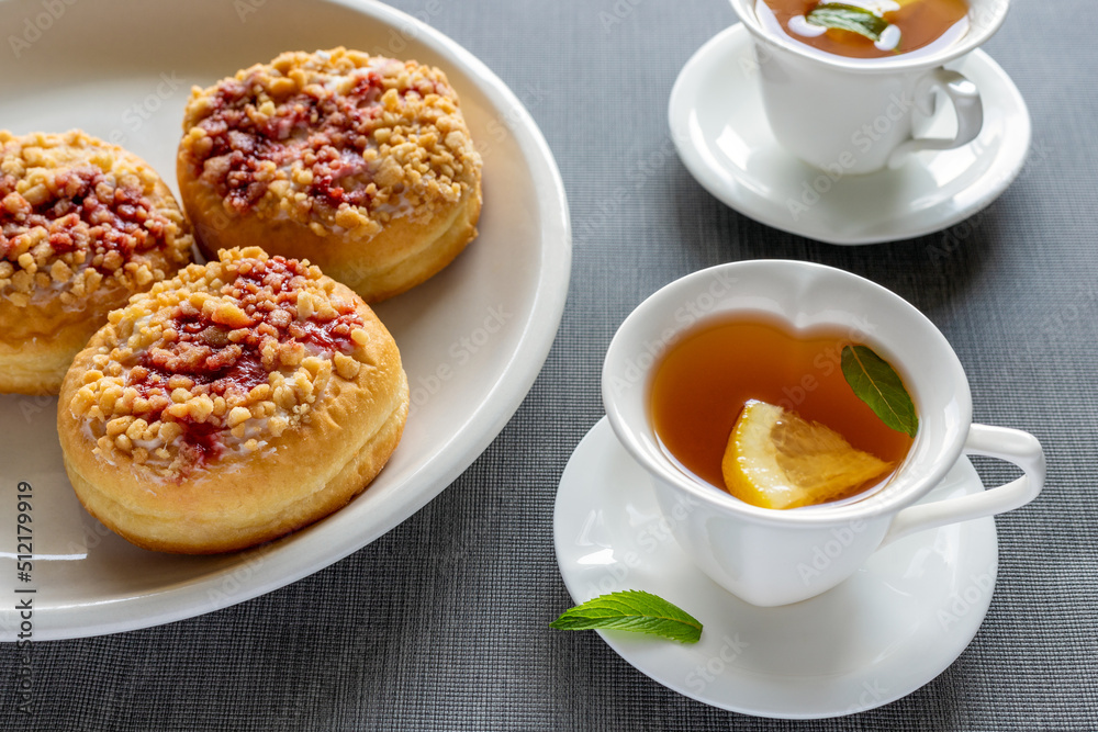 Sweet donuts on plates and cups with mint tea on grey table. Tasty breakfast. Sweet donuts on plates and cups with mint tea on grey table. Tasty breakfast.