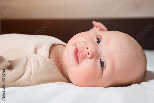 Adorable newborn girl with closed eyes sleeps peacefully in bed. Portrait of little baby with plump cheeks at daytime sleep in nursery, close up