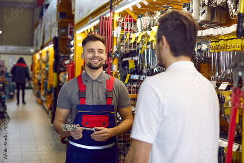 Friendly shop assistant at DIY retail store helping customer choose tools and equipment. Happy smiling salesman helping young man who is buying wrenches and other tools for home repairs photo