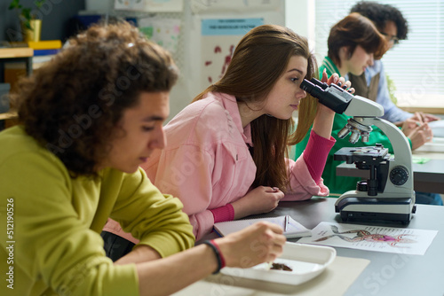 Photos Teenage girl in casualwear studying dissected part of frog in microscope while s