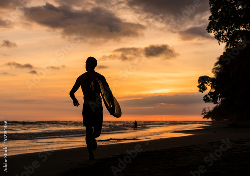 Man carrying surfboard on beach at sunset photo