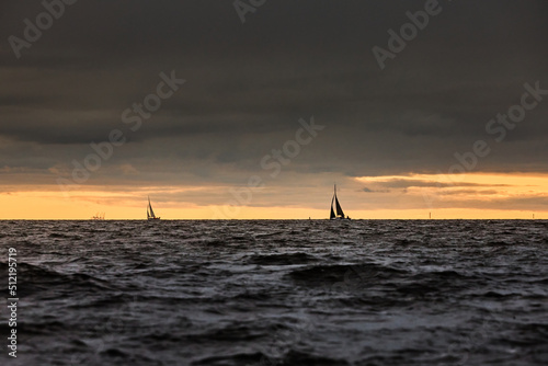 Sailboat in sea at stormy weather, stormy clouds sky orange sky, sail regatta, reflection of sail in the water, bigl waves of water, 