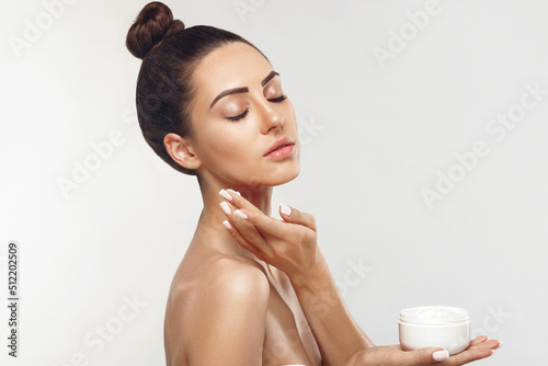 Beauty Woman Concept. Skin care. Portrait of female model holding and applying cosmetic moisturizing cream and touch own face. Nude make-up. Skin Protection. Dermatology