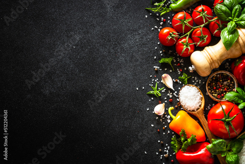 Food background on black stone table with vegetables, herbs and spices. Top view with copy space.
