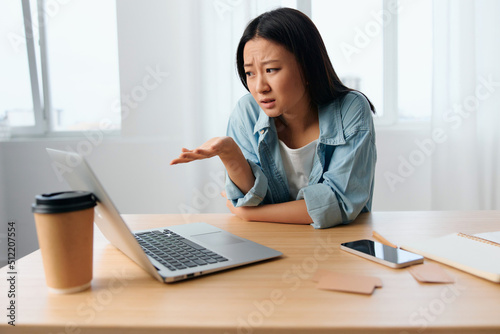 Unhappy confused young Asian cute female businesswoman hates operation problems with laptop in light office interior. Freelancer work at home. Lady corporation leader concept. Copy space Banner Offer © SHOTPRIME STUDIO