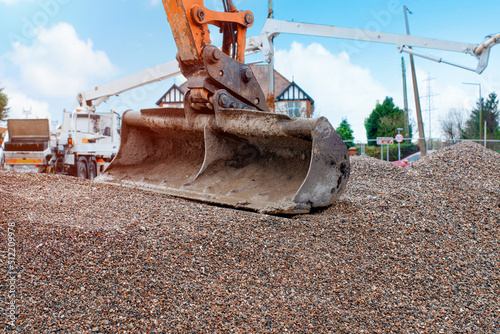 Photos Excavator bucket on top of gravel with concrete pump in background awaiting conc