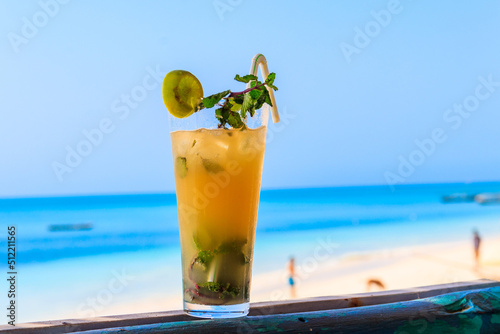 Glass of fresh orange mojito cocktail by the ocean