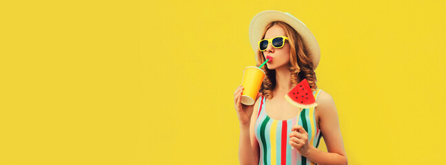 Summer colorful portrait of beautiful young woman drinking juice with lollipop or ice cream shaped slice of watermelon wearing straw hat on yellow background, blank copy space for advertising text