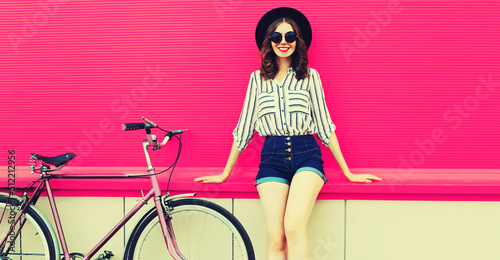 Summer colorful portrait of happy smiling young woman with bicycle in the city on pink background