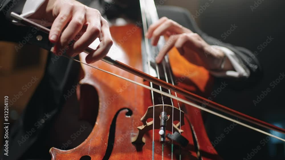 cellist is playing cello on scene of music hall, closeup view, rehearsal or concert of symphonic orchestra