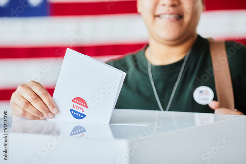 Closeup of woman putting ballot in bin against USA banner background, copy space photo