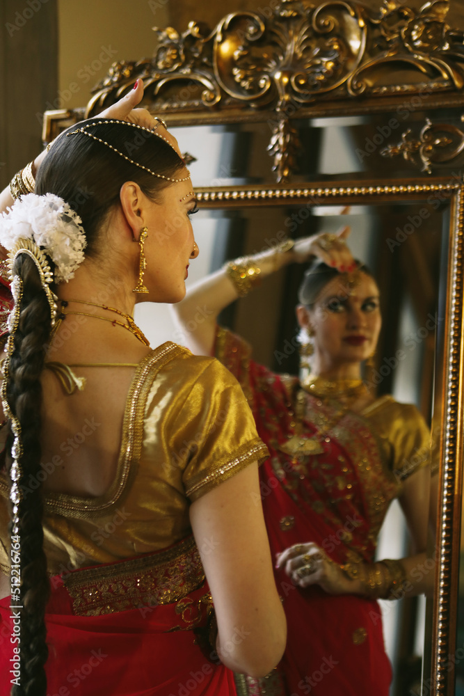 Female model Hindu Bride in saree, wearing gold and jasmine flower garlands in the hair near mirror
