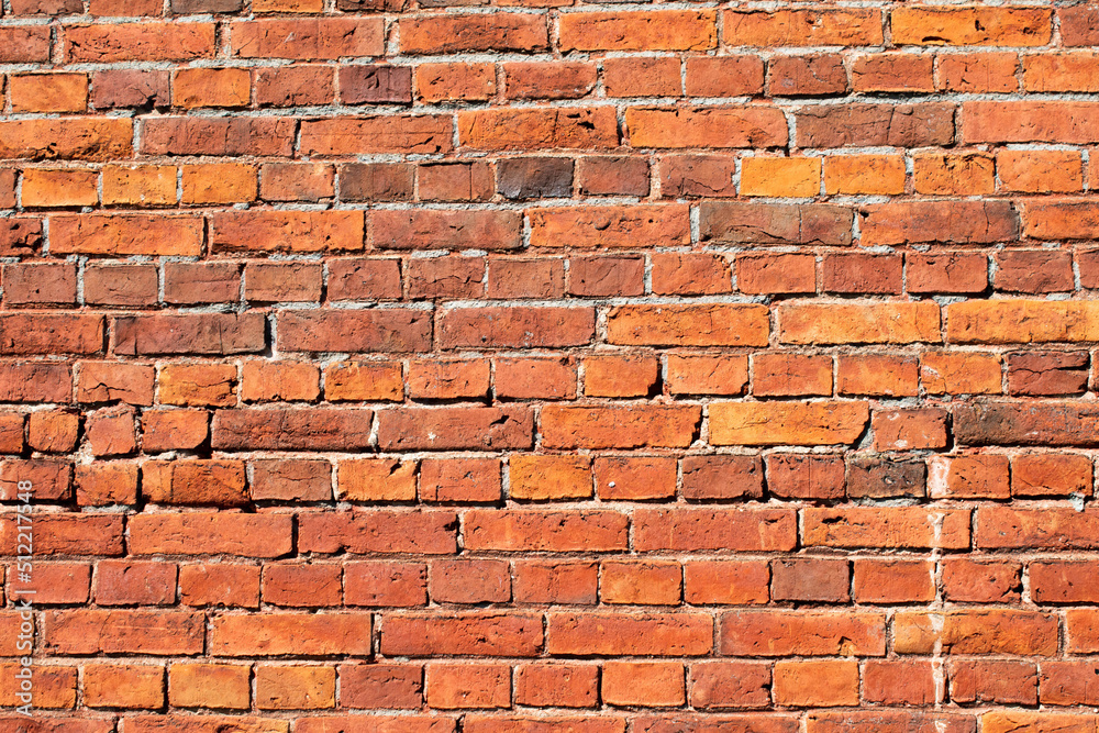 Fototapeta premium Red brick masonry wall, uneven, broken and black burnt bricks, bright red brick background