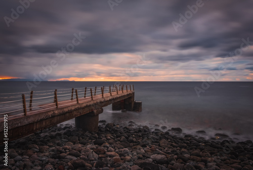 Jetty at pebbles beach near Canico at Portugese Madeira Island at sunrise time. October 2021. Long exposure picture