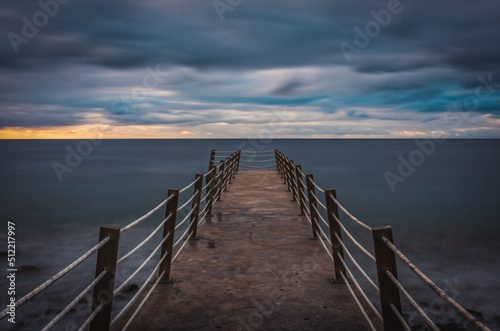 Jetty at pebbles beach near Canico at Portugese Madeira Island at sunrise time. October 2021. Long exposure picture