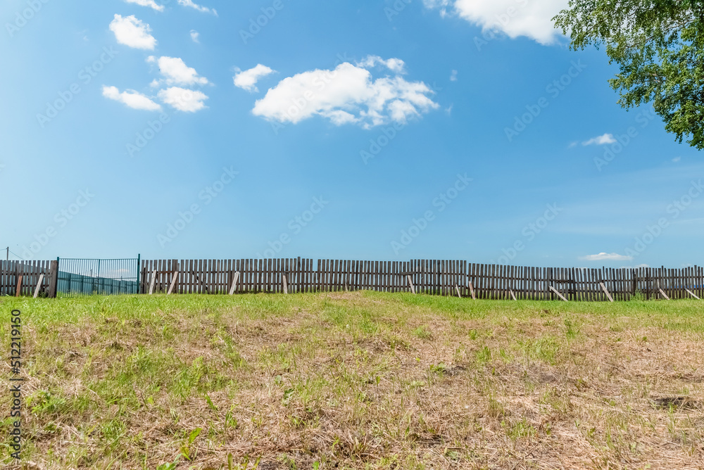 crooked wooden fence with a gate on a farm against the sky