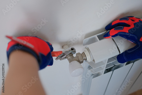 Plumber in protective gloves installing heating radiator in apartment or house photo