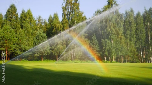 water waters the lawn on the golf course. a rainbow appeared on a sunny day