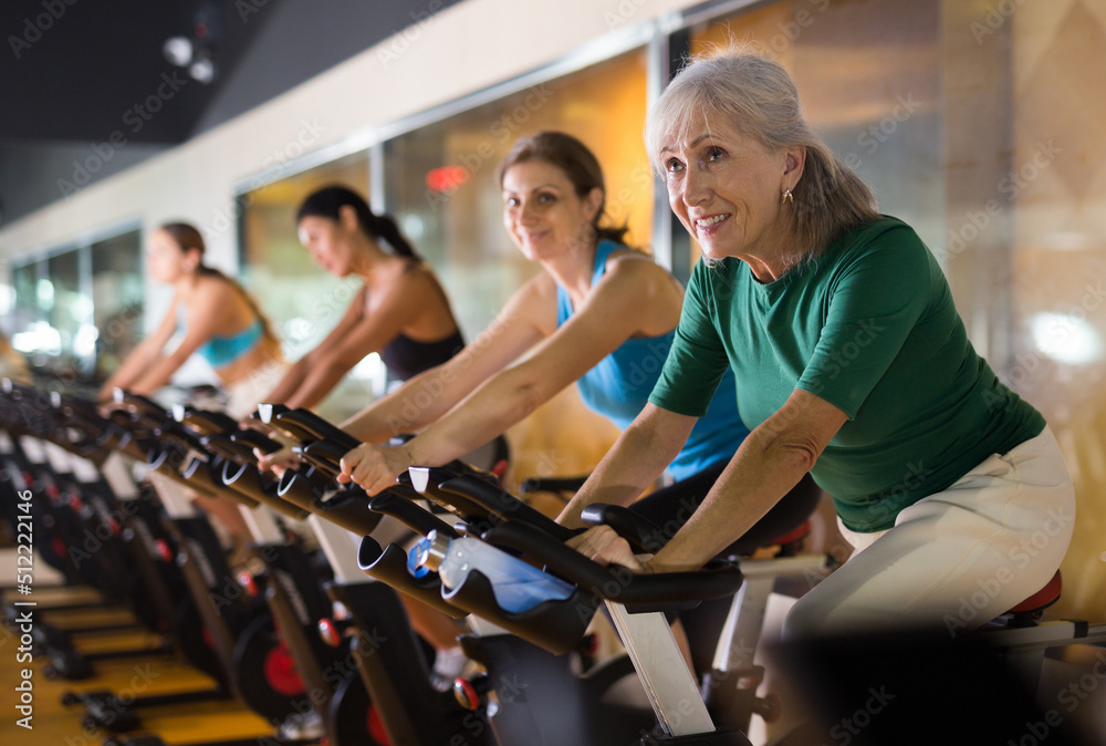 Portrait of confident adult woman training on fitness bike in gym indoor