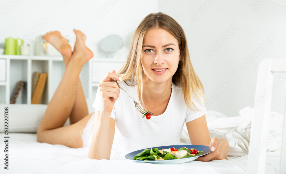 Young beautiful woman eating vegetable salad in her bed