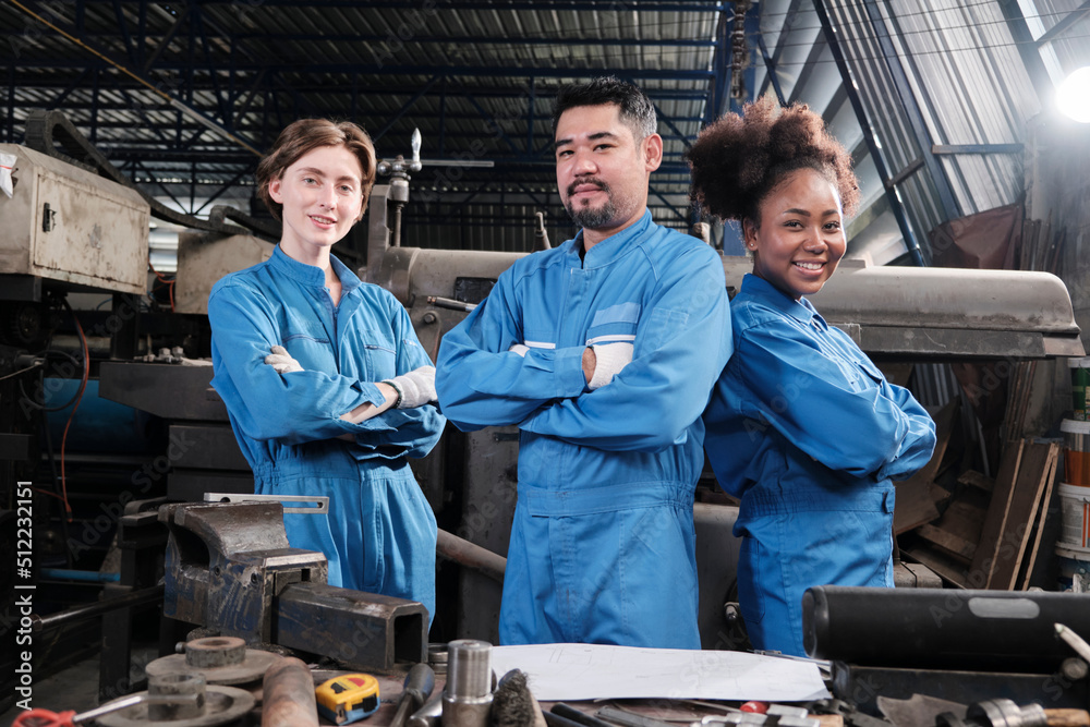 Multiracial industry workers in safety uniforms collaborate with unity, arms crossed, and express happy work together with smile and cheerful in mechanical factory, professional engineer occupation.