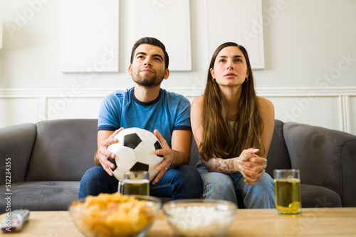 Couple holding a soccer ball while watching the game on tv