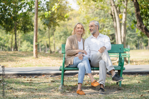 Elderly couple lifestyle concept. Husband embrace wife and sit on seat in the park relax on retirement life.