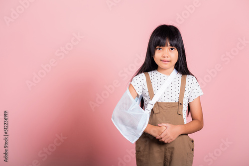 Arm broken. Asian little kid 10 years old hand bone broken from accident with arm splint at studio shot isolated on pink background, Happy child girl accident insurance and extreme sports speed