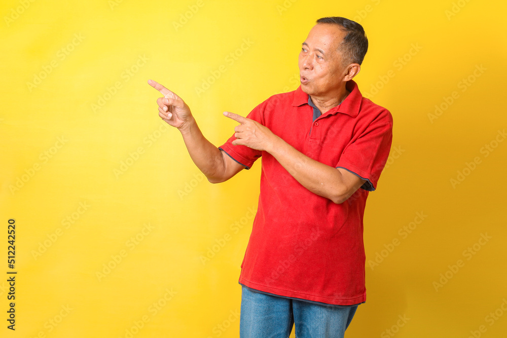 Asian senior man wearing casual t-shirt standing isolated on yellow background pointing with hand and finger up to the side with happy and natural expression on face. Asian senior man wearing casual t-shirt standing isolated on yellow background pointing with hand and finger up to the side with happy and natural expression on face.