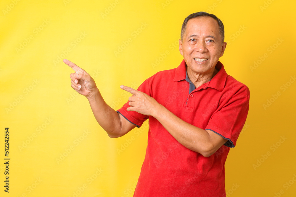 Asian senior man wearing casual t-shirt standing and smiling isolated on yellow background pointing with hand and finger up to the side with happy and natural expression on face. Asian senior man wearing casual t-shirt standing and smiling isolated on yellow background pointing with hand and finger up to the side with happy and natural expression on face.