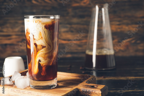 Φωτογραφία Board with glass of cold brew coffee and ice cubes on dark wooden table