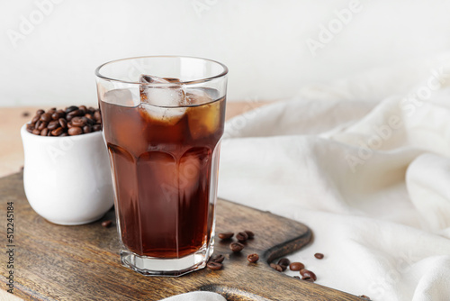 Wooden board with glass of cold brew and coffee beans on table