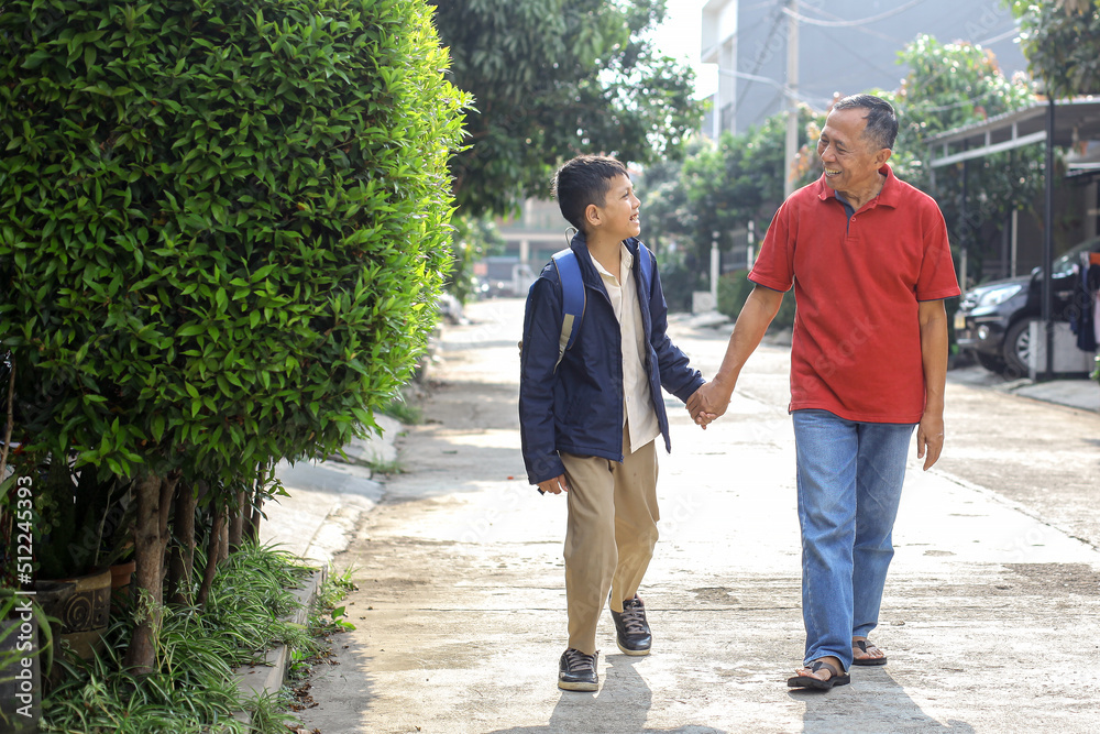 asian boy in uniform and backpack after school is walking together with retirement grandfather. parenting and family activity concept. asian boy in uniform and backpack after school is walking together with retirement grandfather. parenting and family activity concept.