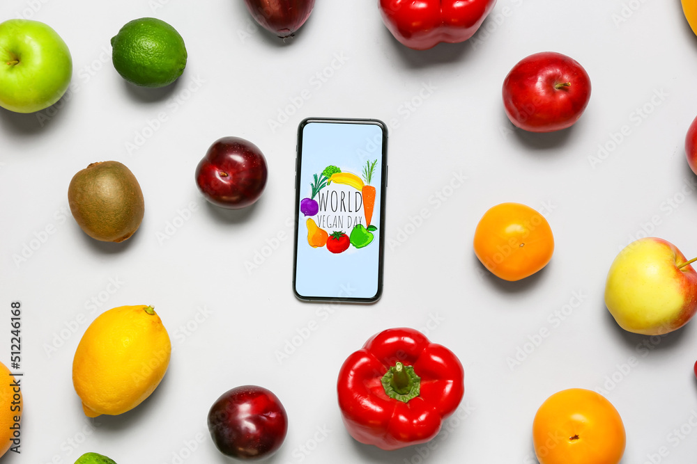 Fresh fruits, vegetables and mobile phone with text WORLD VEGAN DAY on grey background