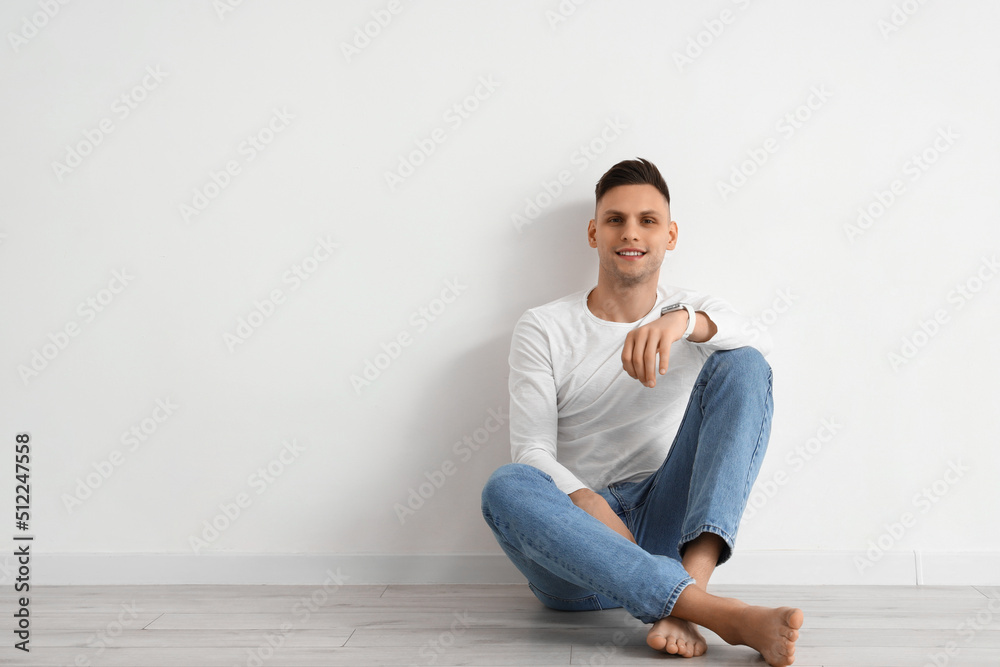 Young barefoot man with smartwatch sitting near light wall Young barefoot man with smartwatch sitting near light wall