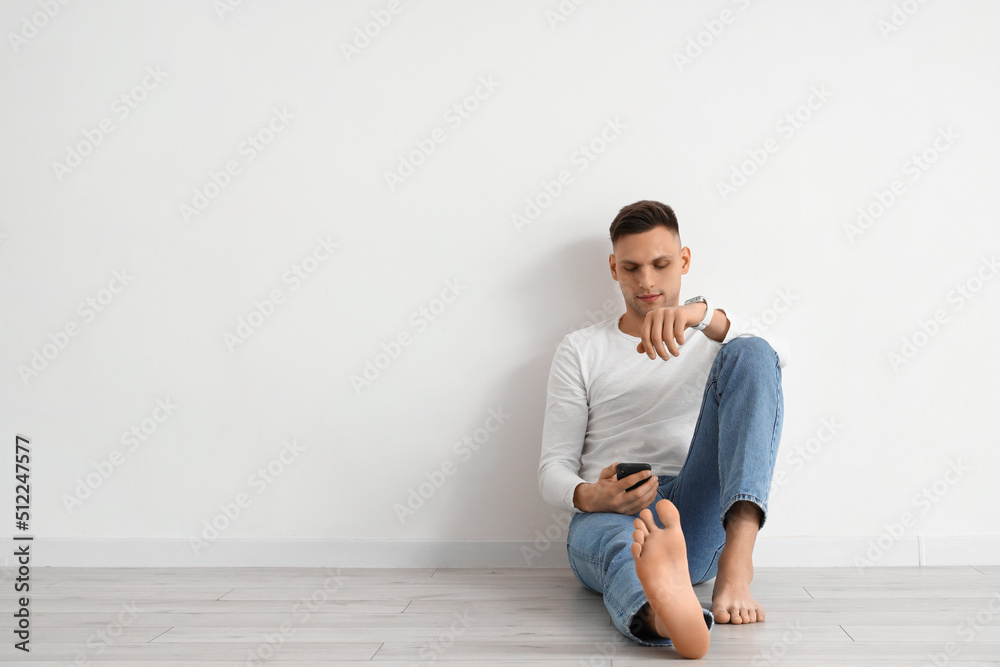 Young barefoot man using mobile phone near light wall Young barefoot man using mobile phone near light wall