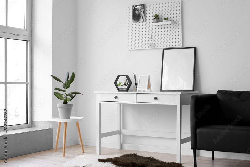Table with blank frames, reed diffuser and planter near light wall in room - obrazy, fototapety, plakaty 