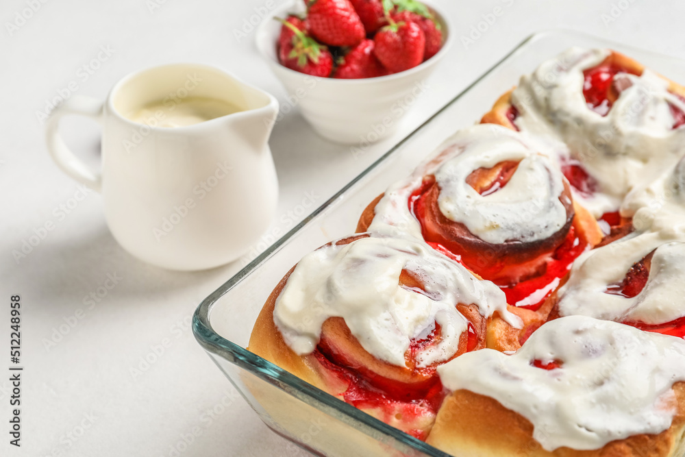 Baking dish with strawberry cinnamon rolls and cream on white background, closeup