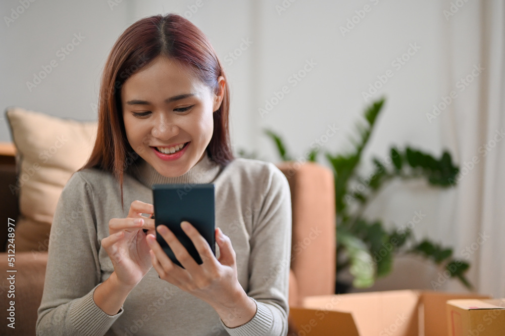 Happy millennial Asian female using her modern cellphone to chat with someone. Happy millennial Asian female using her modern cellphone to chat with someone.