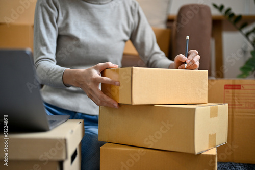 Female online shopping store owner packing a delivery box, writing a customer address © bongkarn