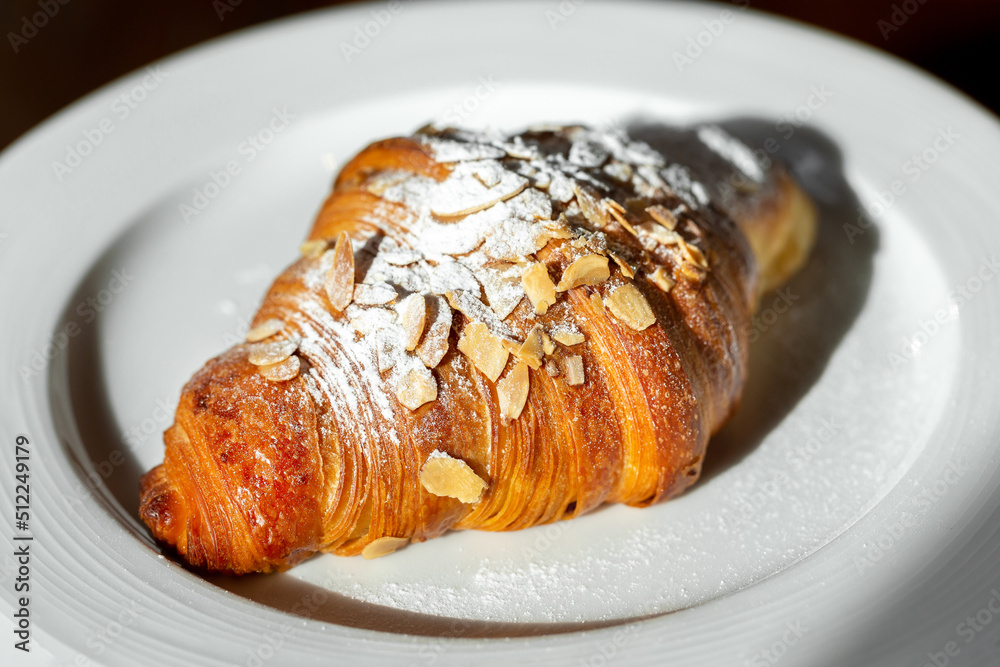 Delicious fresh almond croissant on a white plate, perfect addition to the morning coffee