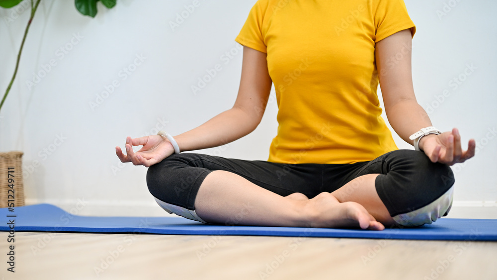 A female sits on yoga mat, practicing lotus yoga pose, meditating at home.
