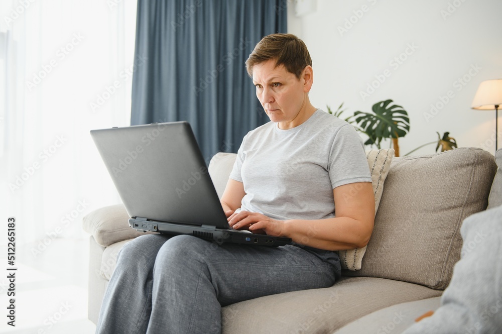 Elderly female sit on couch holding on lap laptop search information, check or typing e-mail, spend time on-line, modern tech, easy interesting pastimes services for retired older generation concept.
