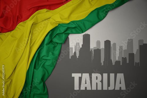 abstract silhouette of the city with text Tarija near waving national flag of bolivia on a gray background. photo