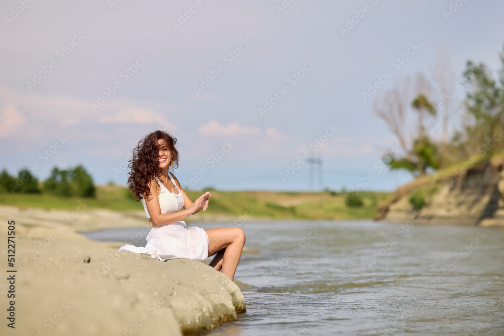 Beautiful woman in white dress on the bank of a river in summer.