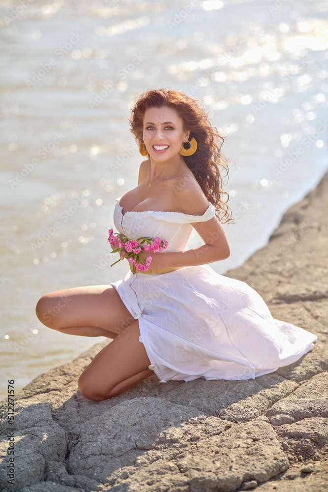 Beautiful woman in white dress on the bank of a river in summer.