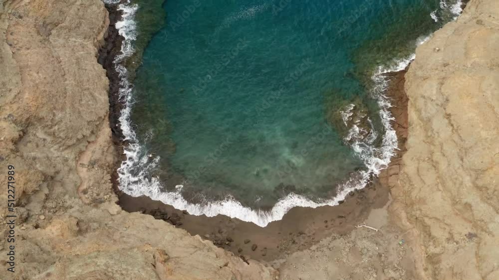 Drone view over a small yellow sand beach, surrounded by rocky mountains and a calm sea Drone view over a small yellow sand beach, surrounded by rocky mountains and a calm sea