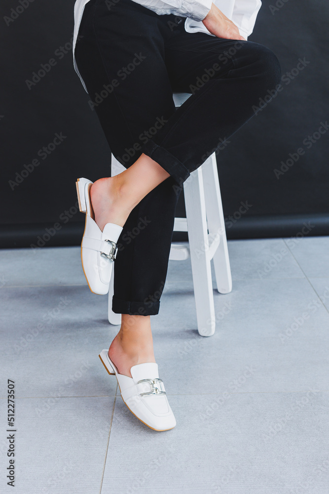 White female leather slippers close-up on female legs. New collection of women's summer leather shoes. White female leather slippers close-up on female legs. New collection of women's summer leather shoes.